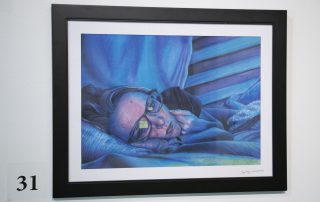 A woman lies on her side in a bed. A reflection in her glasses suggests she is looking at a glowing screen. The entire scene is tinted with a blue glow suggesting that there is no natural light in this photo. Her expression appears lethargic or melancholy.